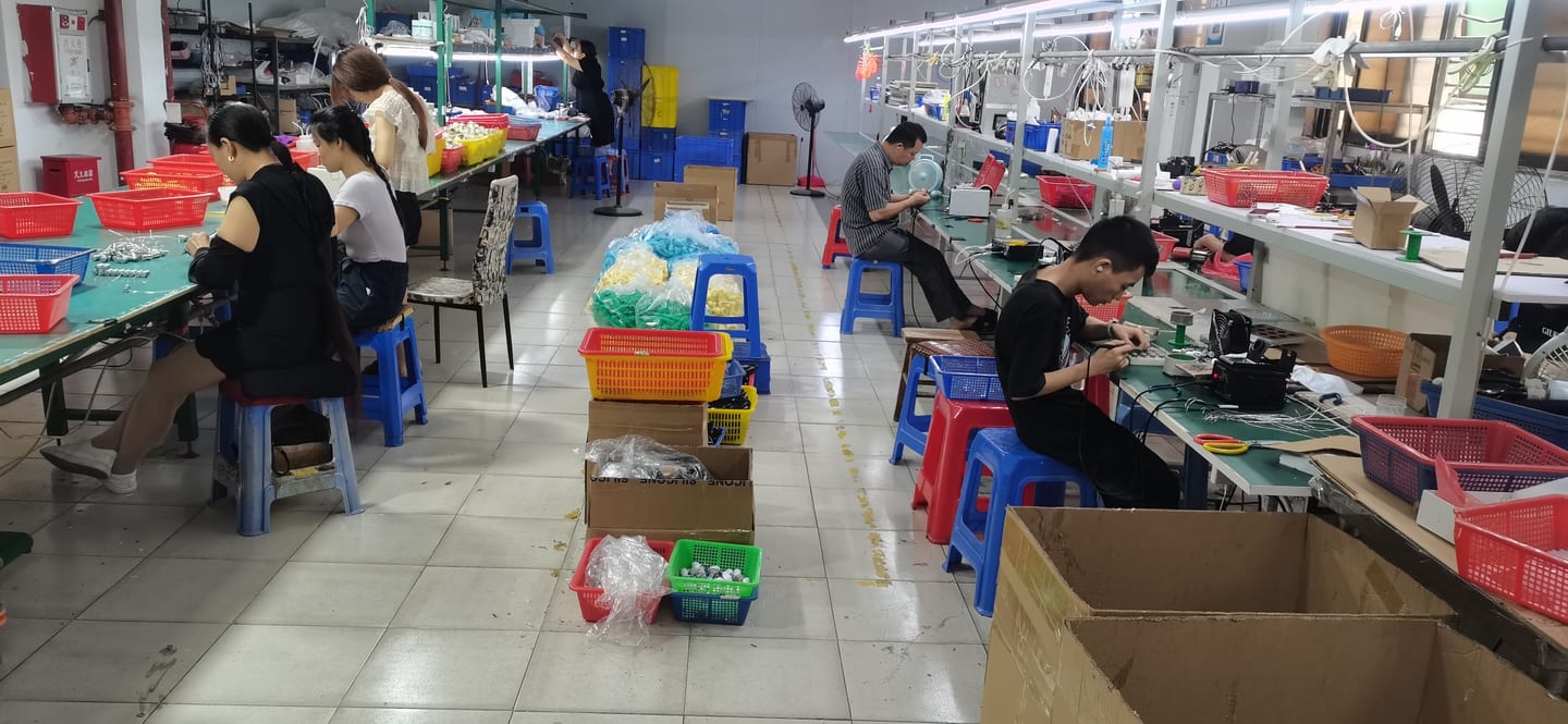 Production floor second angle — assembly workers and material preparation benches